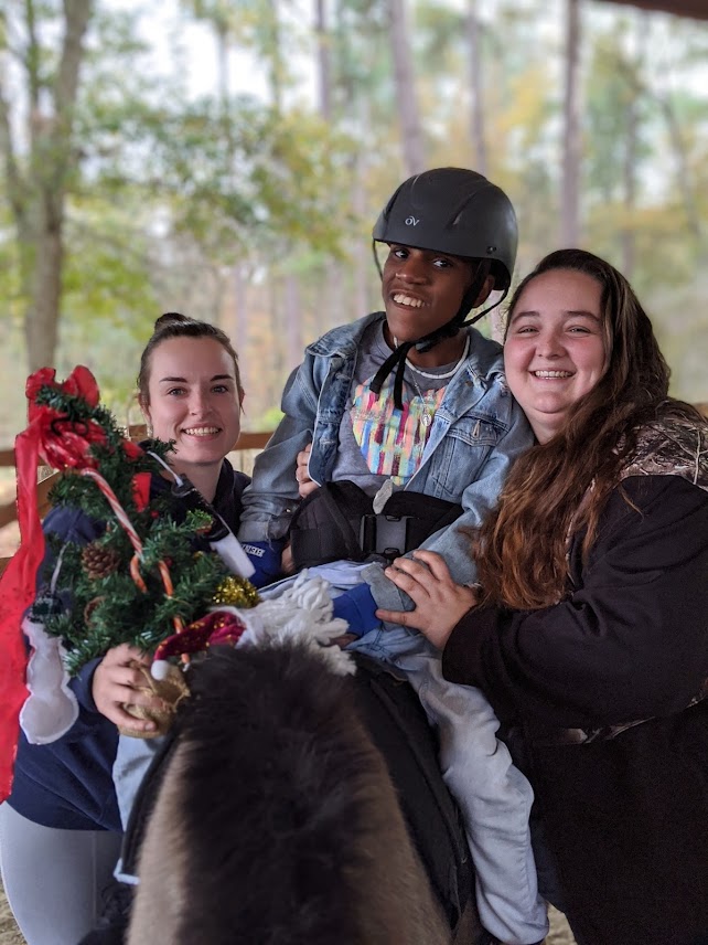 a young person sits on a horse with two staff members on either side